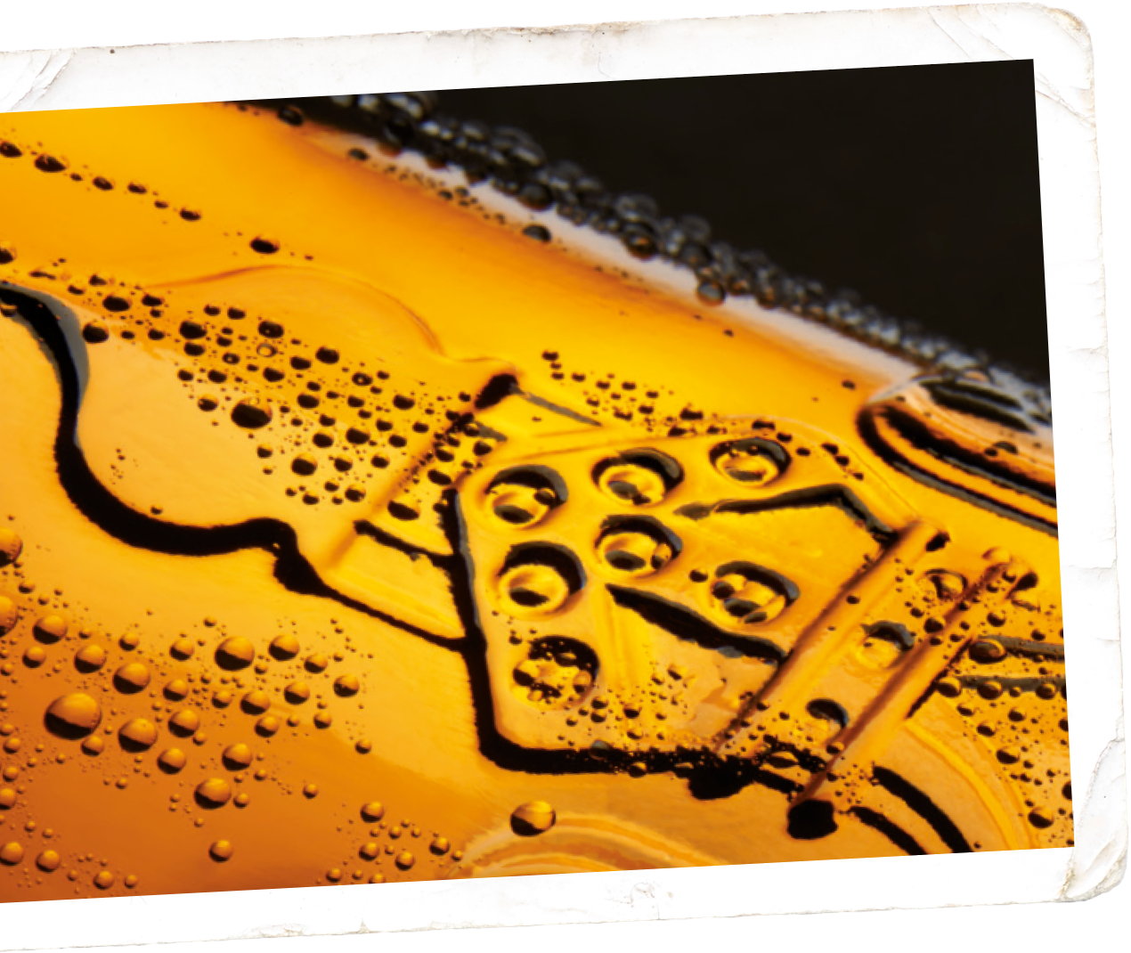 Nahaufnahme von orangenen Flüssigkeitstropfen auf einer strukturierten, dunklen Oberfläche.