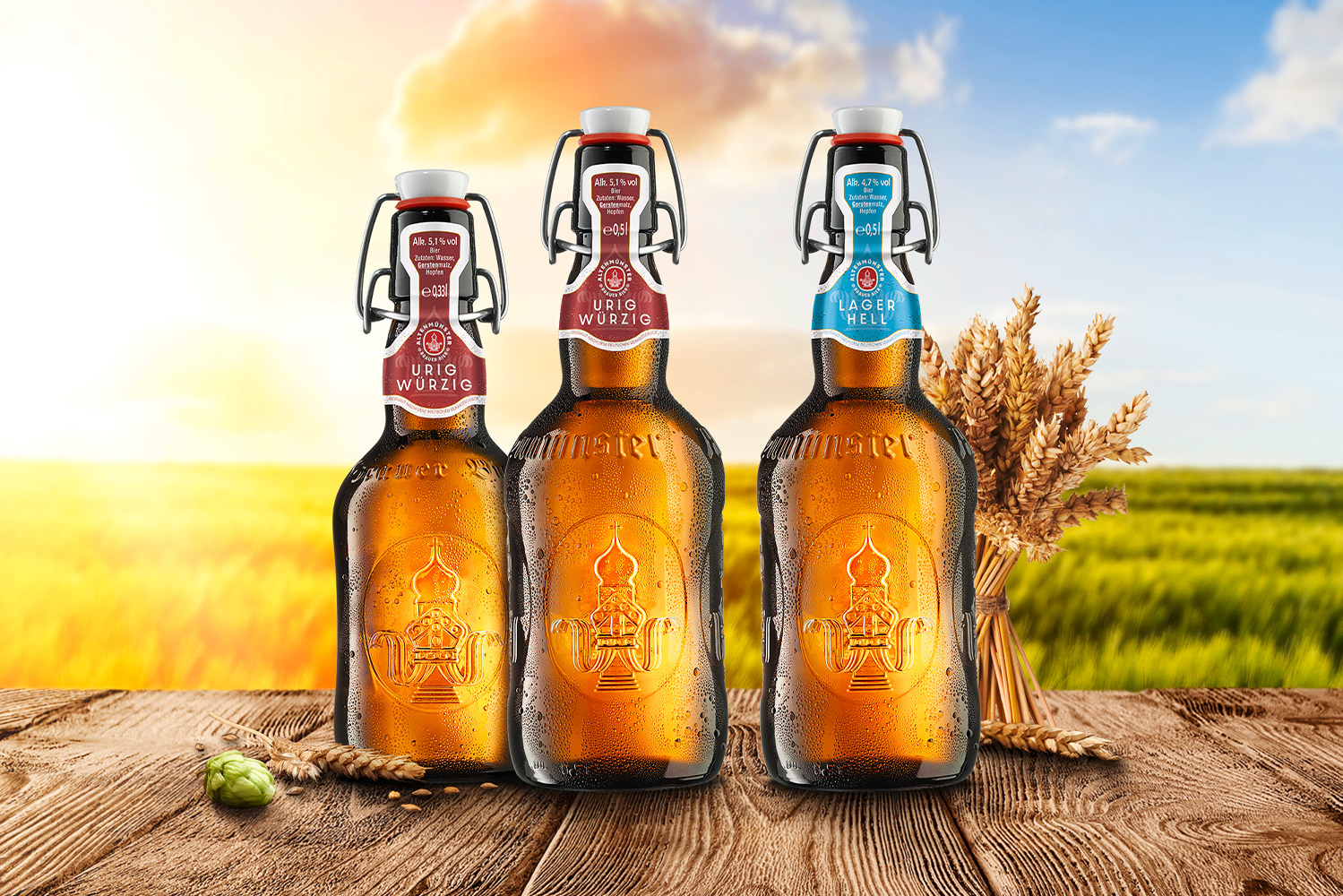 Drei Bierflaschen stehen auf einem Holztisch vor einem Getreidefeld.